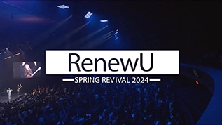 Video Thumbnail of a close up of the back of a few student's heads. One has his arms raised. In front of them you can see the praise and worship team on stage.